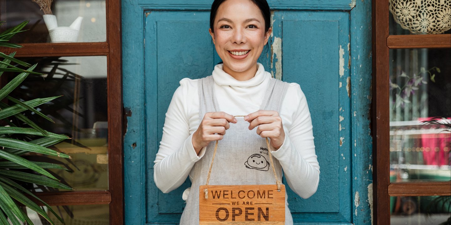 a woman holding a sign that says "welcome we are open"