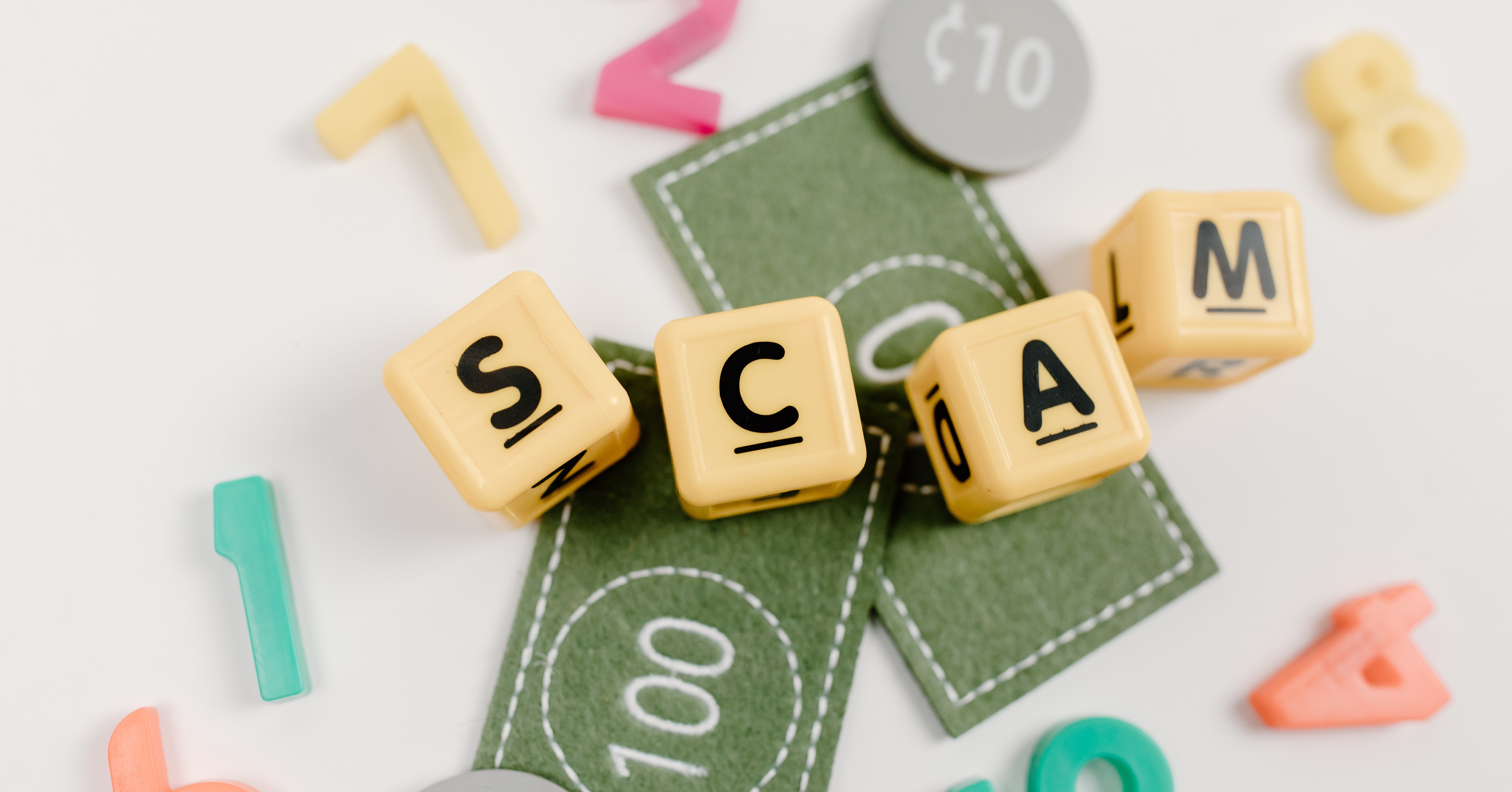 blocks spelling out the word scam on top of play money