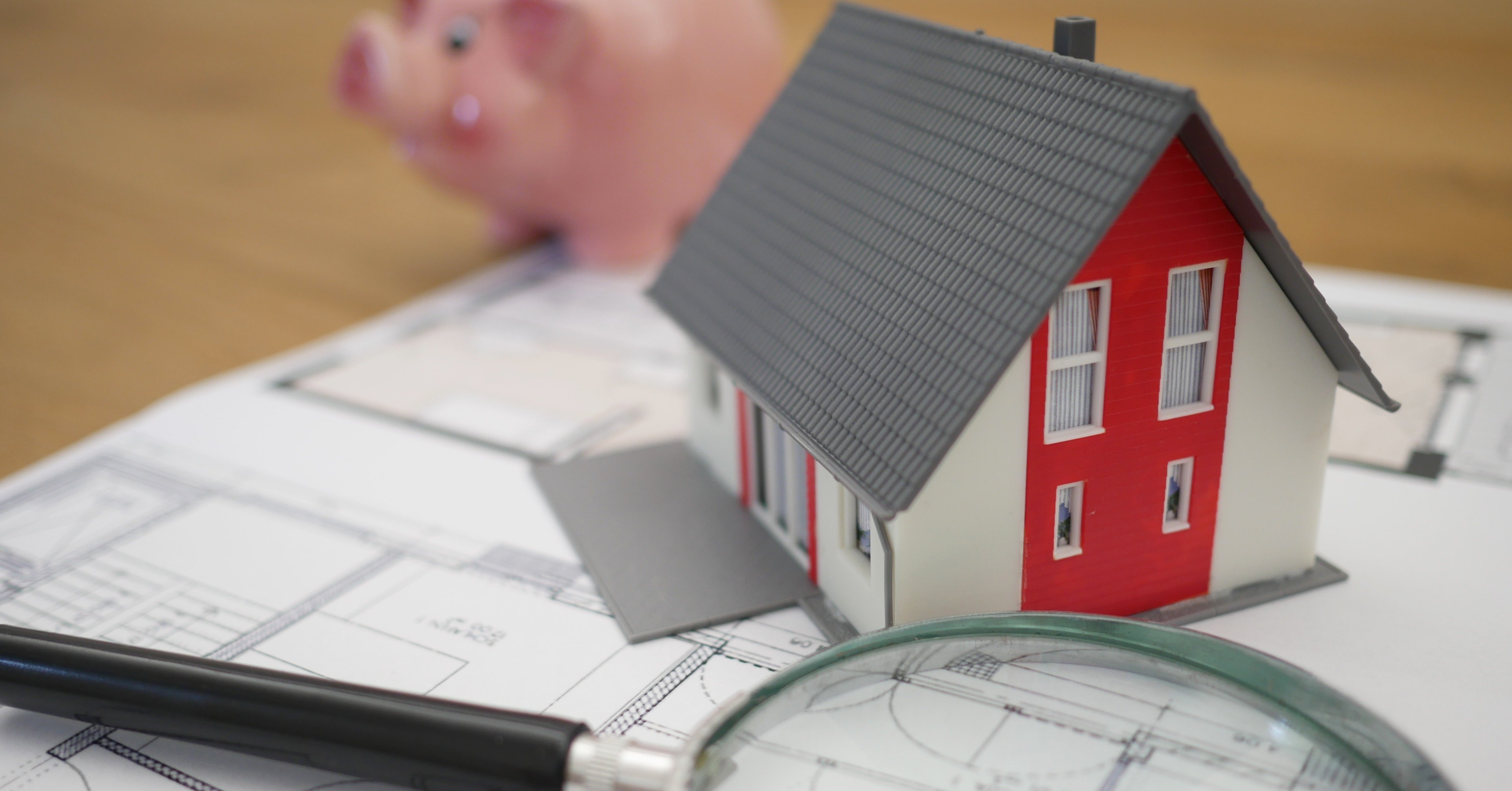 a toy house, a piggy bank, and a magnifying glass sitting on top of building plans